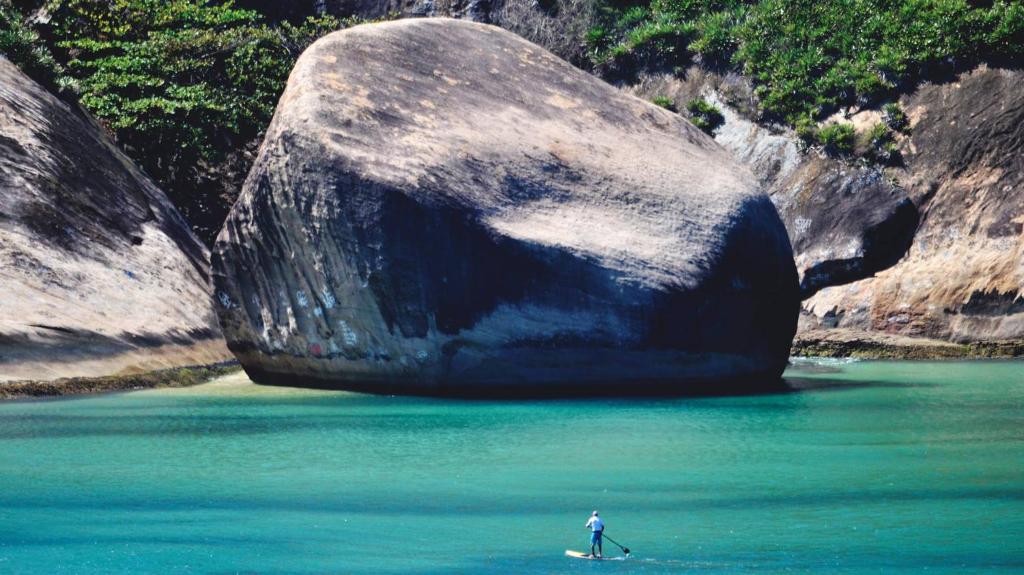 una persona en una tabla de surf en el agua cerca de una gran roca en Rio Way Beach, en Río de Janeiro