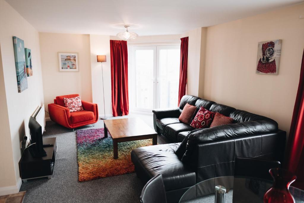 ベルファストにあるComfortable Belfast city centre apartmentのリビングルーム(黒い革張りのソファ、赤い椅子付)