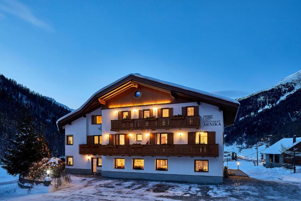 Un grand bâtiment avec des lumières allumées dans la neige dans l'établissement Garni Appartements Arnika, à Sulden