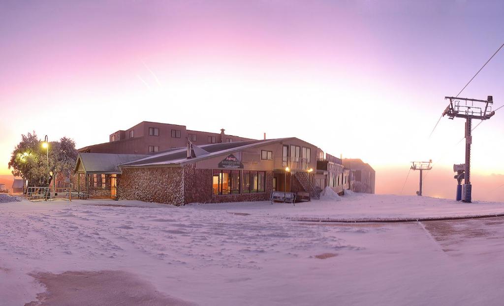 ein Gebäude im Schnee, hinter dem die Sonne untergeht in der Unterkunft Arlberg Hotel Mt. Buller in Mount Buller