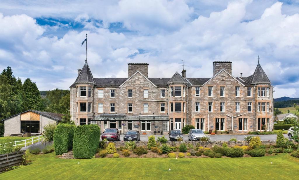 un gran edificio con coches estacionados frente a él en The Pitlochry Hydro Hotel, en Pitlochry