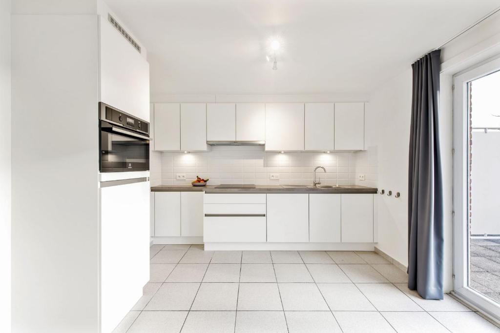 een witte keuken met witte kasten en een tegelvloer bij Dream apartment for work stay in Oostrozebeke