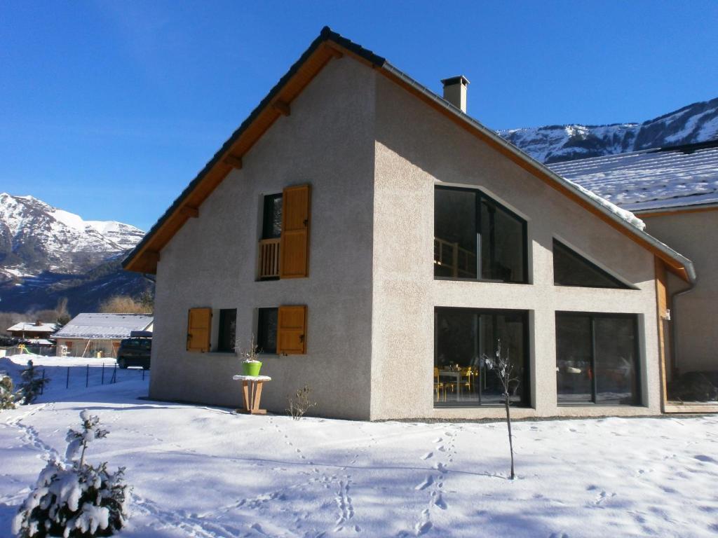 une maison dans la neige avec des montagnes en arrière-plan dans l'établissement Le Perce-Neige - Petite Piscine - Jardin - Gîtes - ALPES HUEZ, à Le Vert