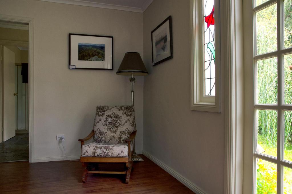 Zimmer mit einem Stuhl, einer Lampe und Fenstern in der Unterkunft Gellibrand River Gallery Accommodation in Gellibrand