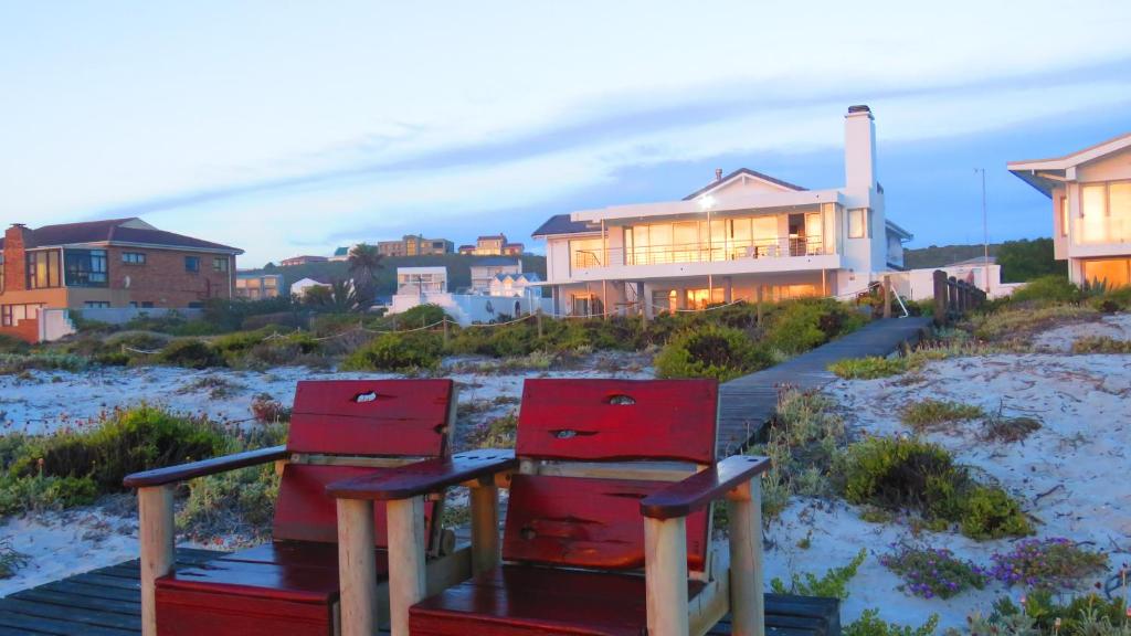 two red chairs sitting on a boardwalk next to houses at On The Beach Apartments in Yzerfontein