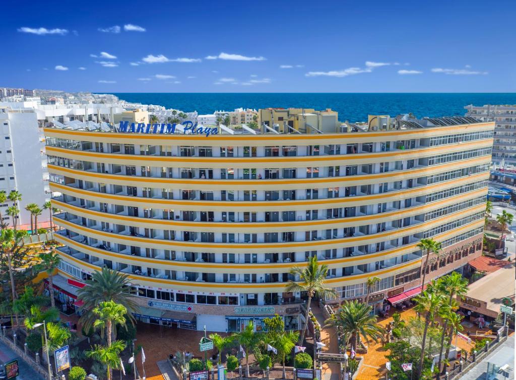 um grande edifício amarelo com palmeiras em frente ao oceano em Maritim Playa em Playa del Inglés