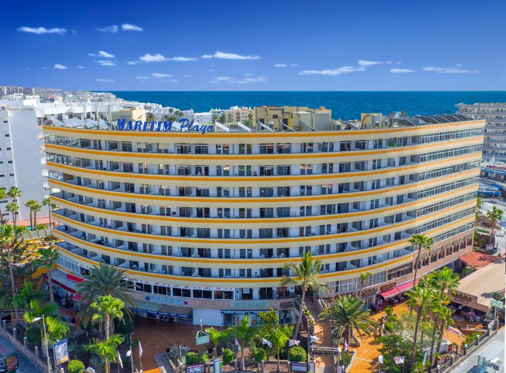 a large yellow building with palm trees in front of the ocean at Maritim Playa in Playa del Ingles