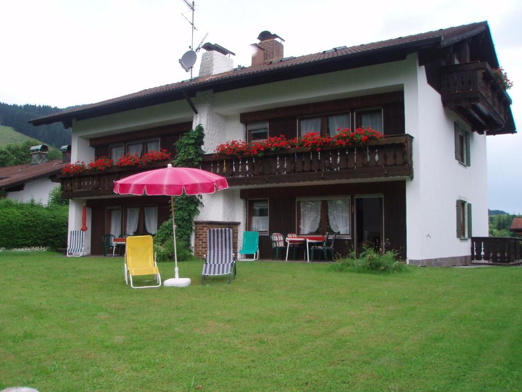 ein Haus mit einem rosa Regenschirm und Stühlen im Hof in der Unterkunft Haus Sorgschrofen in Pfronten