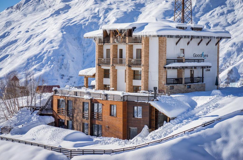 a building in the snow with a mountain behind it at Hotel GoodAura in Gudauri