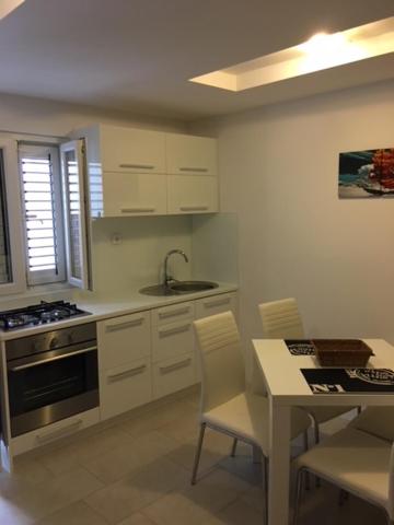 una cocina con armarios blancos y una mesa con sillas. en Apartman Bombon en Selce