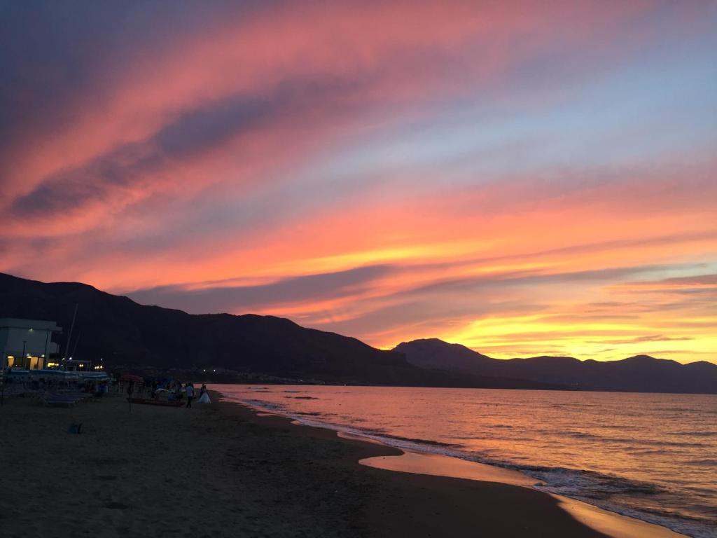 un tramonto sulla spiaggia con persone che camminano sulla spiaggia di Casa Vacanze Playa 54 a Castellammare del Golfo