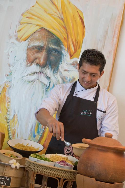 a man is preparing food in front of a painting at Code Samui Hotel in Mae Nam