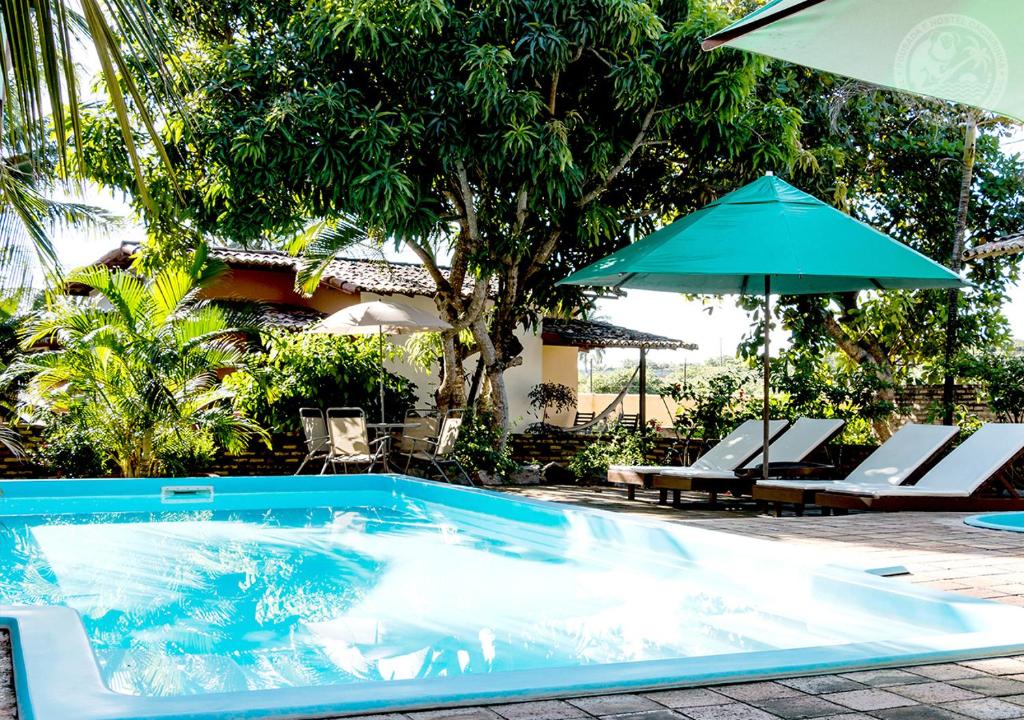 a swimming pool with an umbrella and chairs and a table at Pousada Cacimbinha - ePipa Hotéis in Pipa