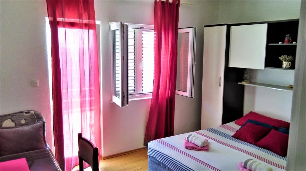 a bedroom with pink curtains and a bed and a chair at Apartment Vesna in Milna