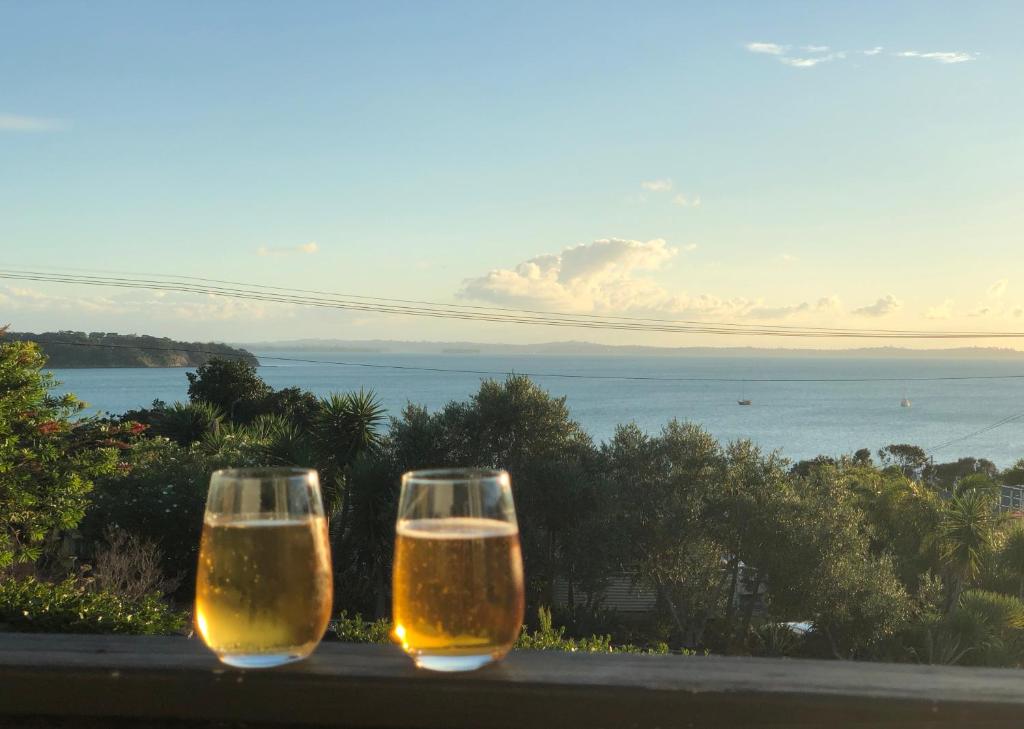 two glasses of beer sitting on a ledge with the ocean at The Black Pearl, Waiheke Island in Oneroa