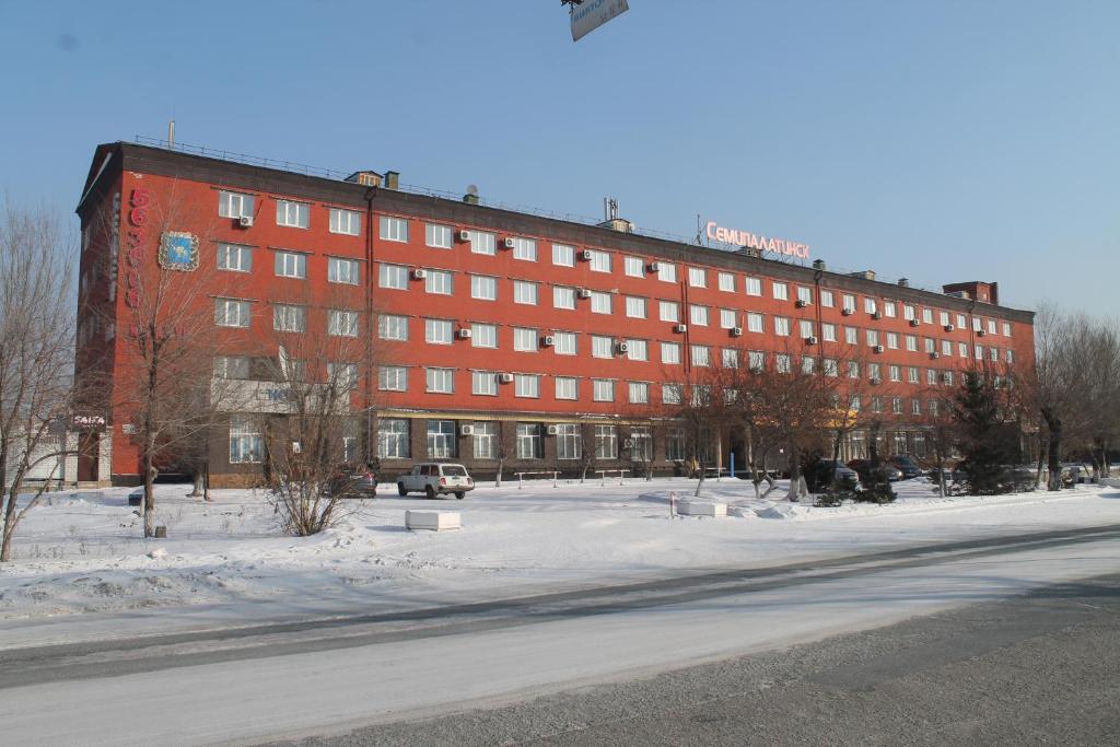 duży czerwony budynek w śniegu przed ulicą w obiekcie Semey Hotel w mieście Semej