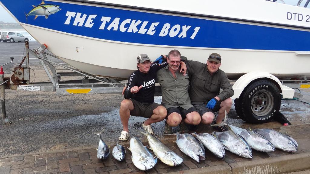 three men kneeling next to a bunch of fish next to a boat at Breakerview in Shelly Beach