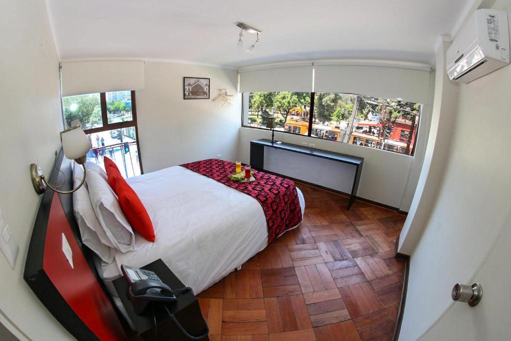 a bedroom with a bed and a desk and two windows at Hotel Plaza Ñuñoa in Santiago
