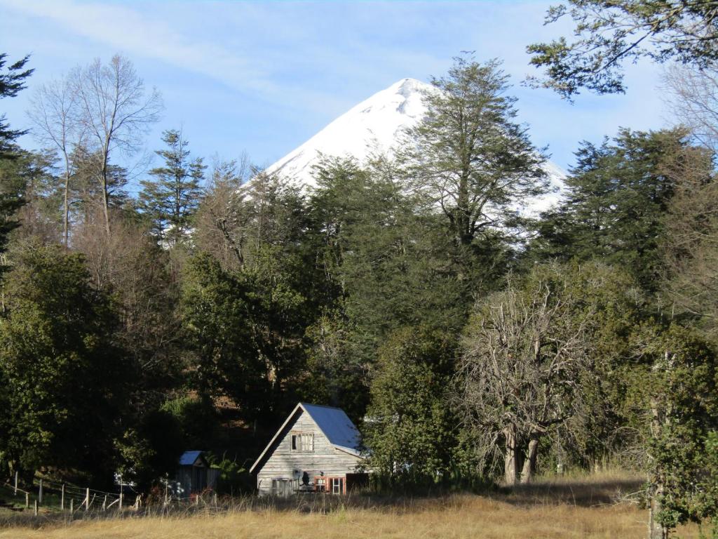 una casa vieja frente a una montaña cubierta de nieve en Refugio Montaña Kultrun Mawida, Habitación con baño y cocina privada, en Curacautín