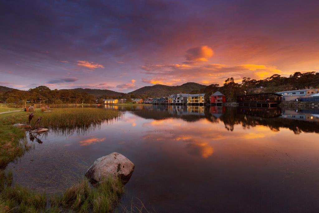 Lake Crackenback Resort & Spa في كراكينباك: تجمع كبير للمياه مع غروب الشمس في الخلفية