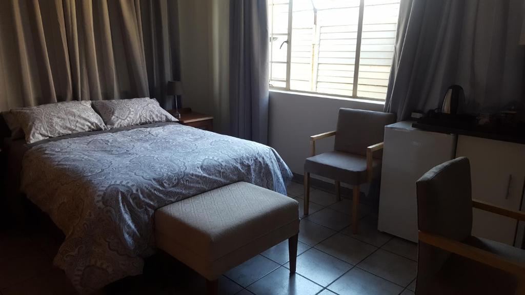 a bedroom with a bed and a chair and a window at Pretoria Inn in Pretoria