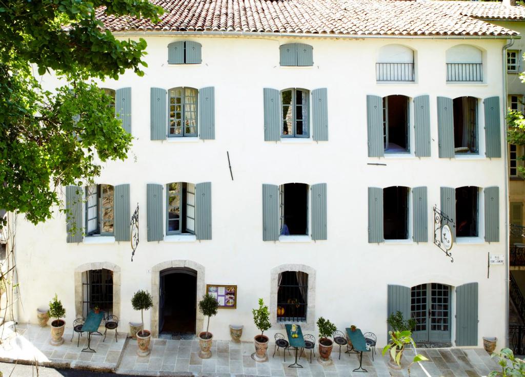 uma casa branca com persianas verdes, mesas e cadeiras em Hotel Restaurant des Deux Rocs em Seillans