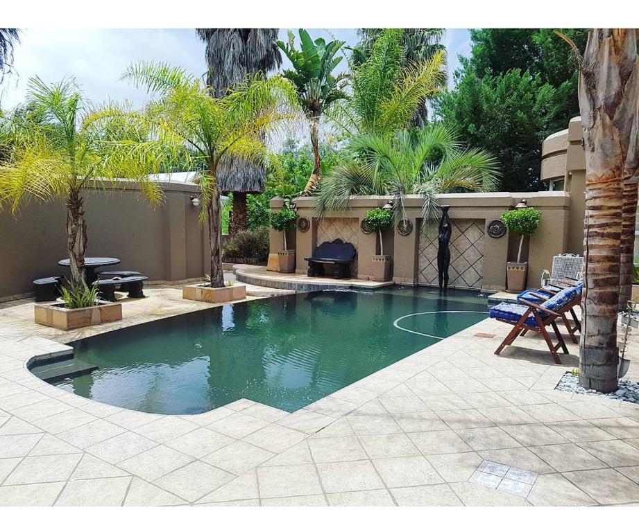 a swimming pool in a yard with palm trees at Oudtshoorn Guest House in Oudtshoorn