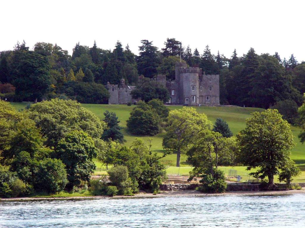 a castle on a hill with trees and a body of water at Clydebank Apartment in Glasgow