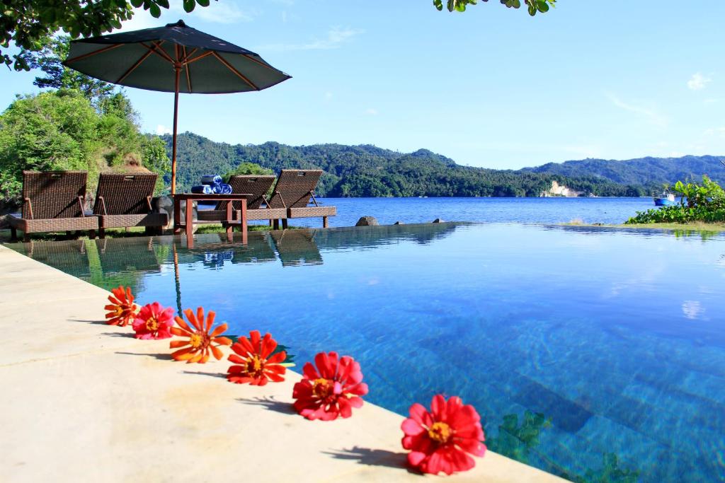 a swimming pool with red flowers and an umbrella at Cocotinos Lembeh a Boutique Dive Lodge in Bitung