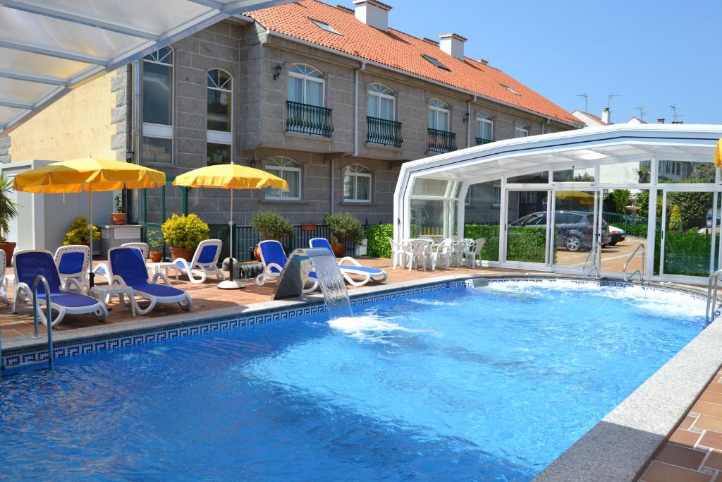 a pool with chairs and umbrellas next to a building at Hotel Playa Compostela in Vilagarcia de Arousa