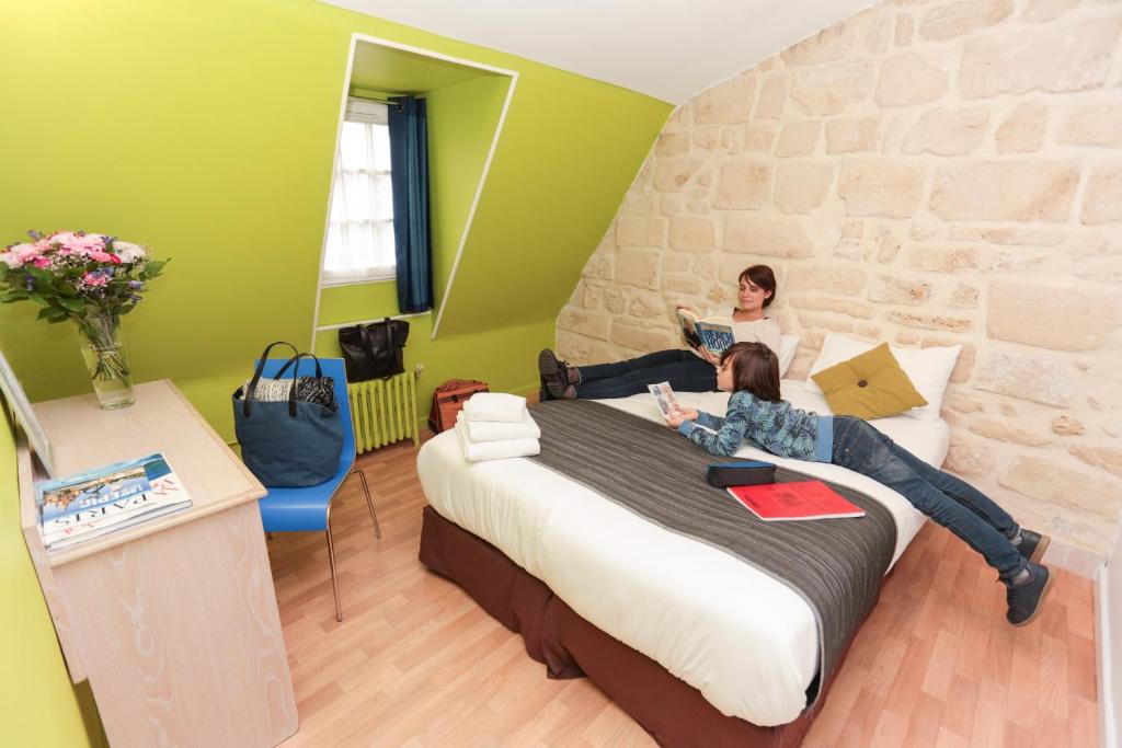 two women laying on a bed in a room at Le Montclair Montmartre by River in Paris