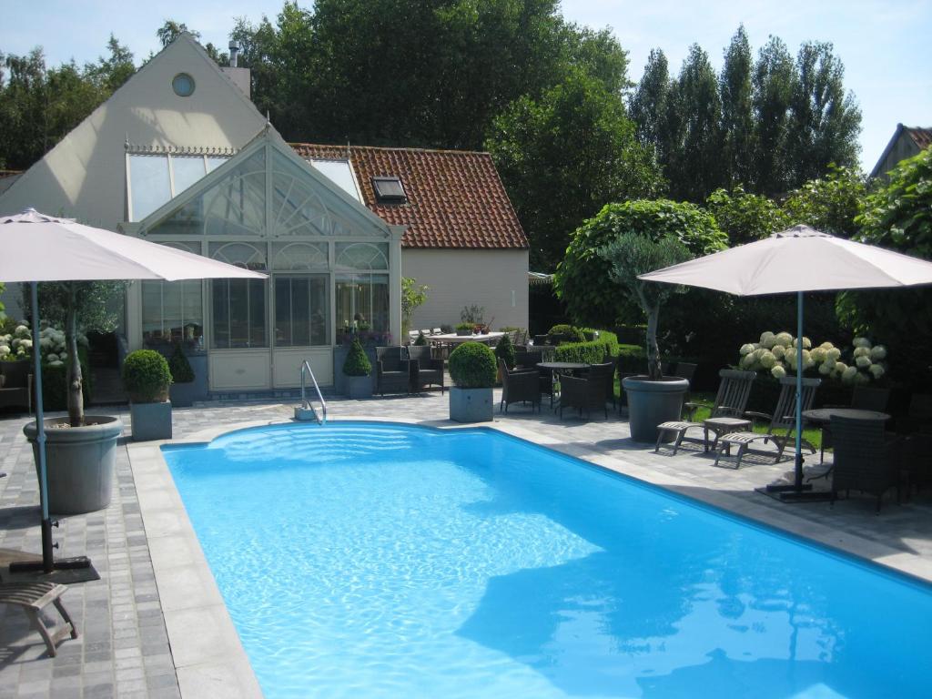 a swimming pool with umbrellas and a house at Boutique hotel Het Bloemenhof in Dudzele