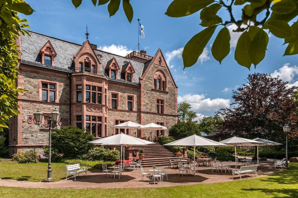 ein Gebäude mit Tischen und Sonnenschirmen davor in der Unterkunft Romantik Hotel Schloss Rettershof in Kelkheim