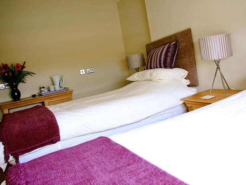 two beds in a hotel room with purple sheets at The Arun View Inn in Littlehampton