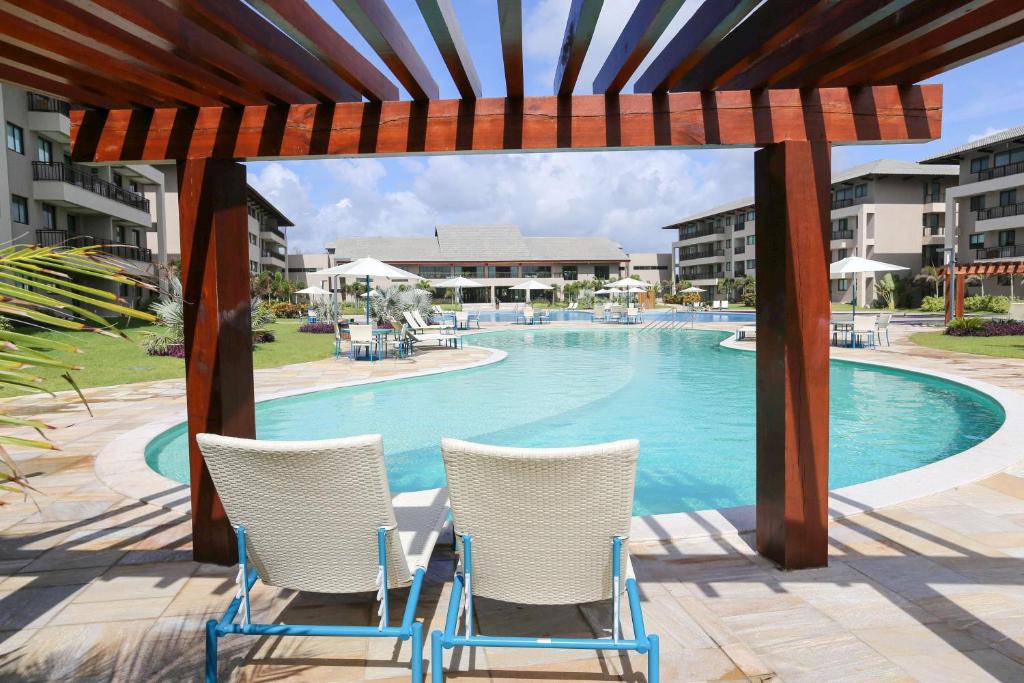 - une piscine avec 2 chaises et une pergola dans l'établissement Beach Class Eco Life Apt 202-A, à Porto de Galinhas