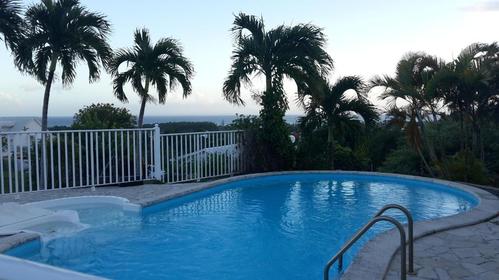 a swimming pool with palm trees and a fence at Les Gîtes Les Hauts de Montmain in Sainte-Anne