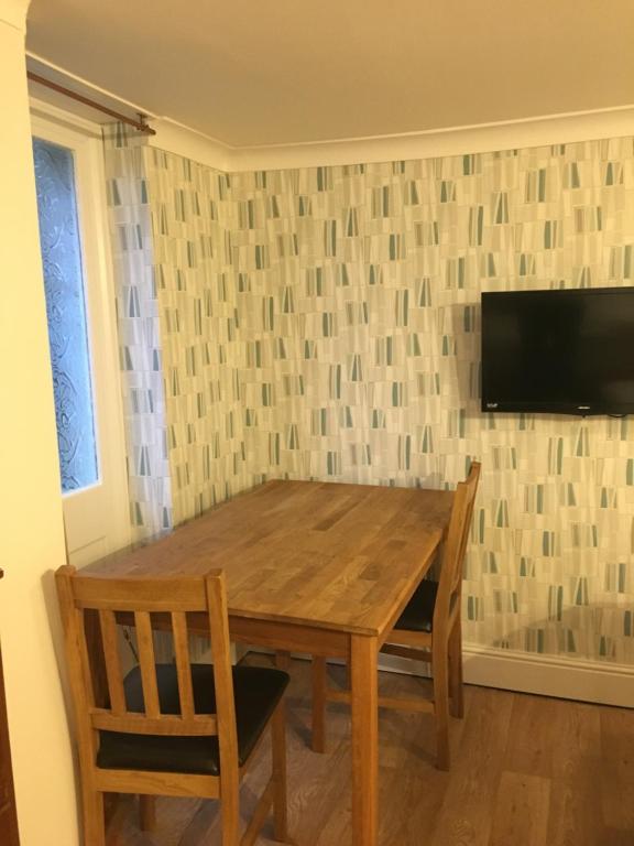 mesa de madera con 2 sillas y TV en la pared en Addison B&B, en Guildford