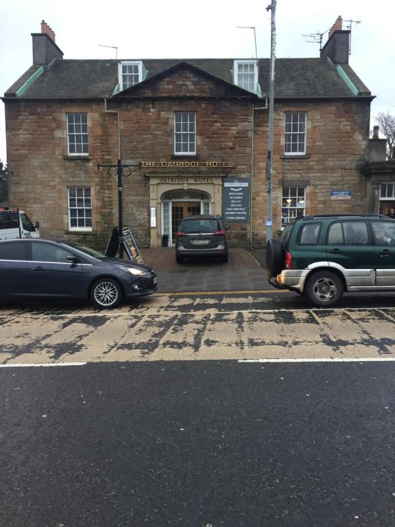 dos coches estacionados frente a un edificio de ladrillo en Oatridge hotel, en Uphall