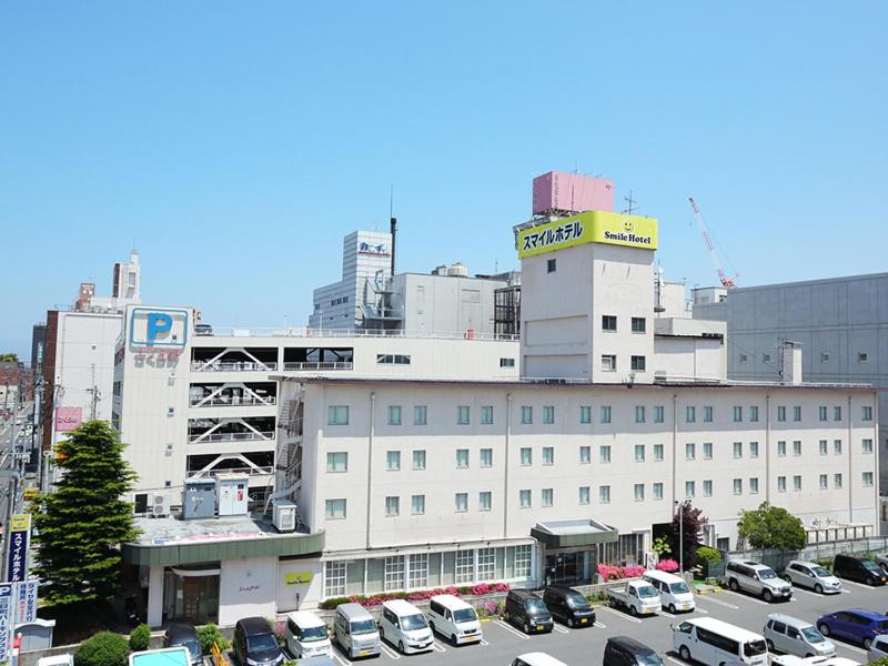 een groot wit gebouw met auto's geparkeerd op een parkeerplaats bij Smile Hotel Hachinohe in Hachinohe
