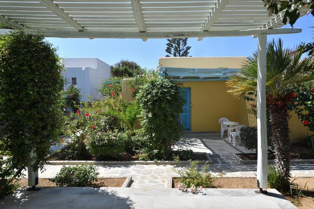 a garden with a white pergola and a yellow house at Surfing Beach Village Paros in Santa Maria