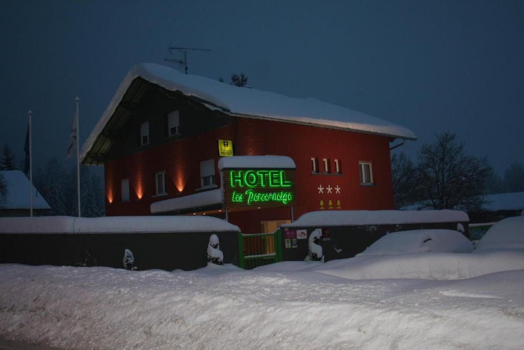 Un bâtiment rouge avec un panneau dans la neige dans l'établissement Hôtel Les Perce-Neige, à Bonnétage