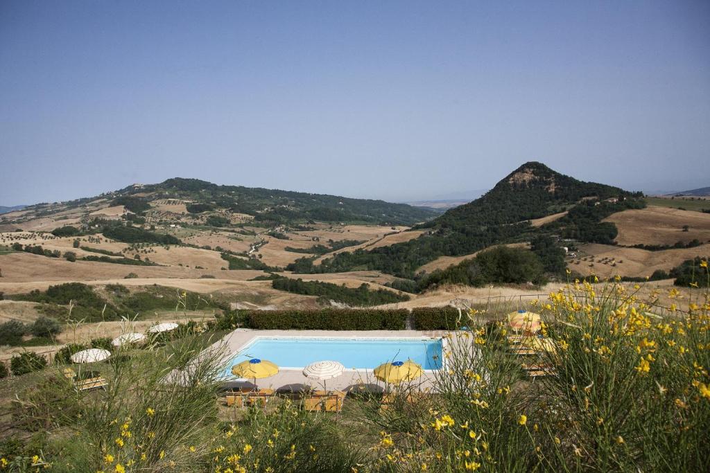 a swimming pool in the middle of a field with mountains at Agriturismo Villa Felice in Volterra