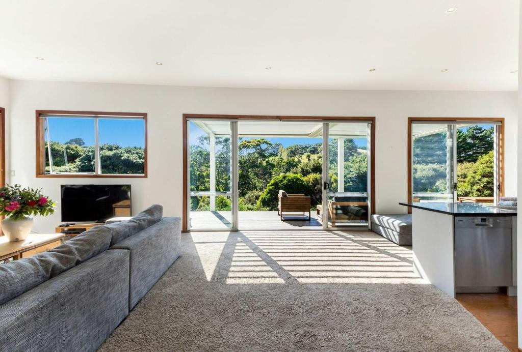 uma sala de estar com um sofá e uma cozinha com portas de vidro deslizantes em Karaka Sanctuary with Spa Pool by Waiheke Unlimited em Oneroa