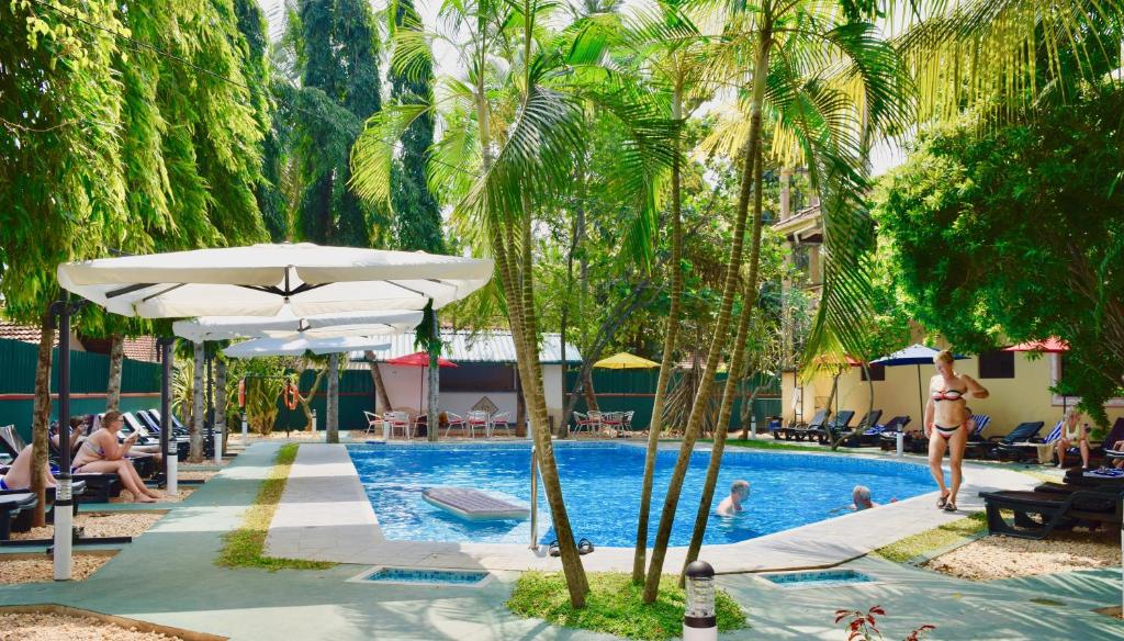 a pool with palm trees and people sitting around it at Rico Shadow Guest House & Restaurant in Wayikkal