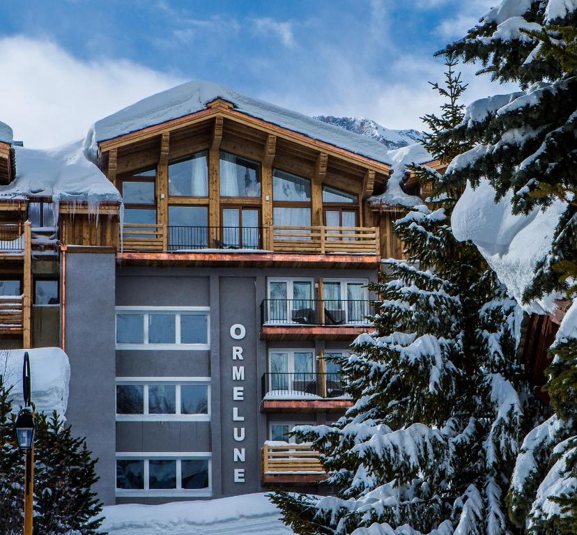 un grand bâtiment avec des arbres enneigés devant lui dans l'établissement Hotel Ormelune, à Val dʼIsère