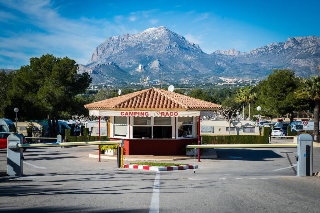 a building in a parking lot with a mountain in the background at Camping Raco in Benidorm