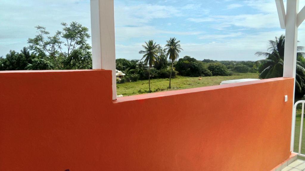 an orange fence with a view of a field and palm trees at Habitation Fouyapen II in Sainte-Anne