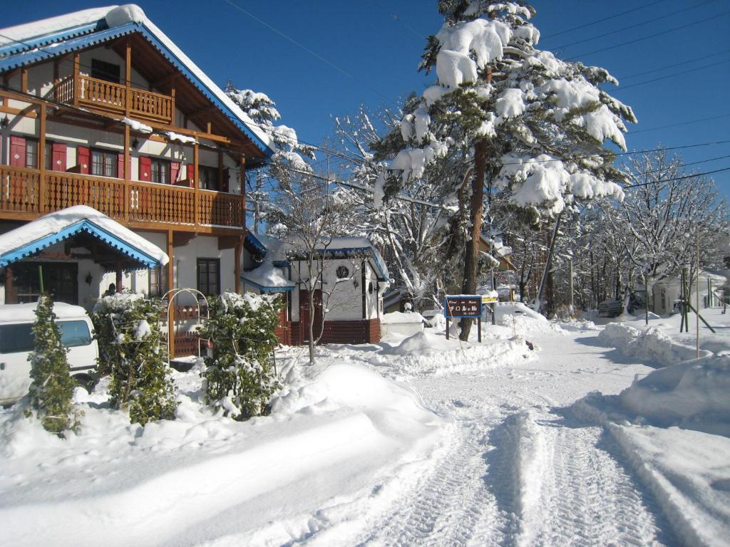 un patio cubierto de nieve con una casa y un árbol en Alpine Wind, en Hakuba