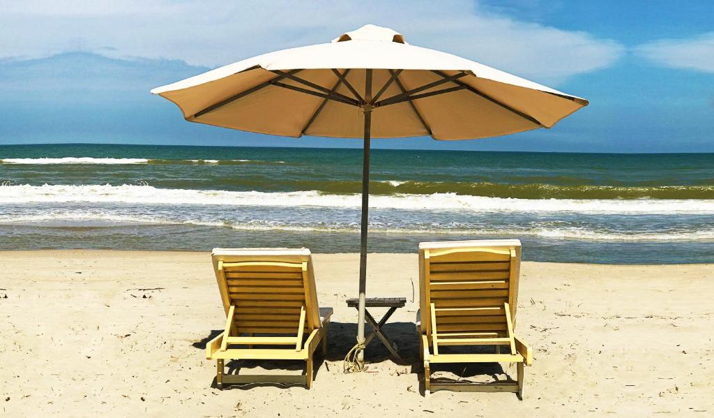 duas cadeiras e um guarda-sol na praia em Co Bon Beachside em Hoi An