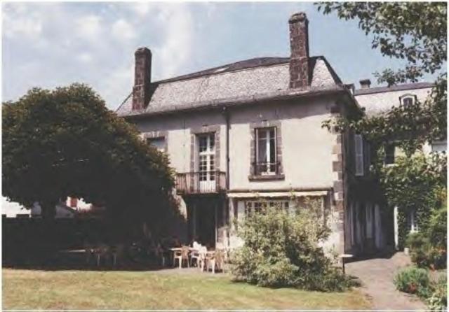 uma grande casa branca com uma mesa em frente em La Source du Mont em Saint-Martin-Valmeroux